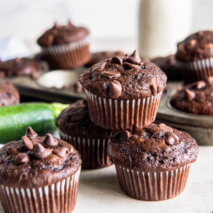 double chocolate zucchini muffins stacked on top of each other in front of zucchini.