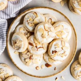 plate of almond sugar cookies with icing and sliced almonds for garnish.