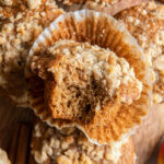 apple cider muffin with a bite sitting on open paper liner on more muffins.