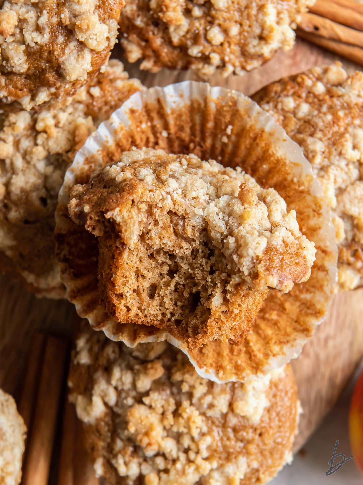 apple cider muffin with a bite sitting on open paper liner on more muffins.