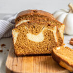 slice of pumpkin cream cheese bread leaning against loaf on wood cutting board.