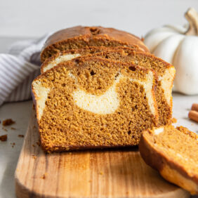 slice of pumpkin cream cheese bread leaning against loaf on wood cutting board.