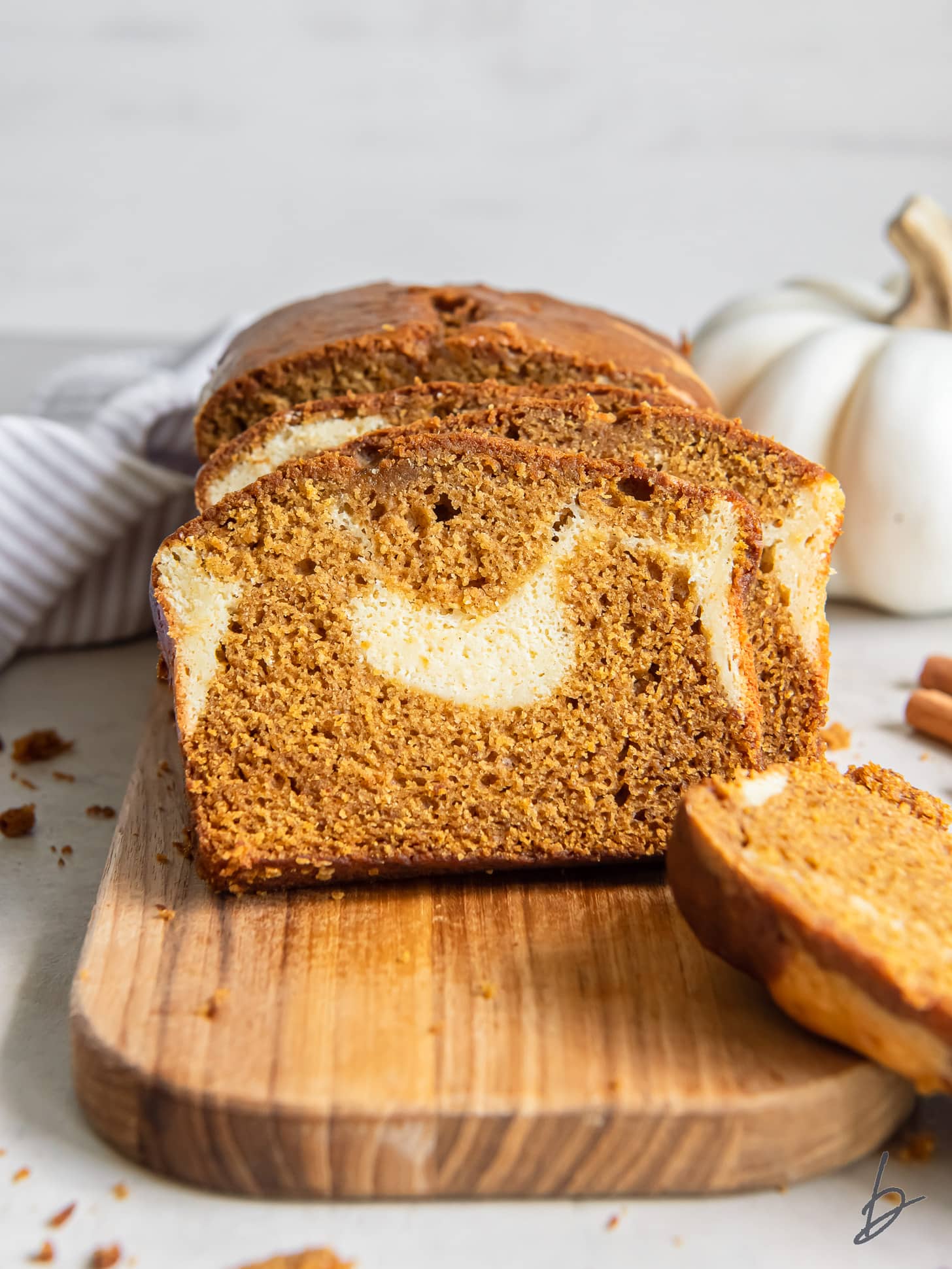 slice of pumpkin cream cheese bread leaning against loaf on wood cutting board.