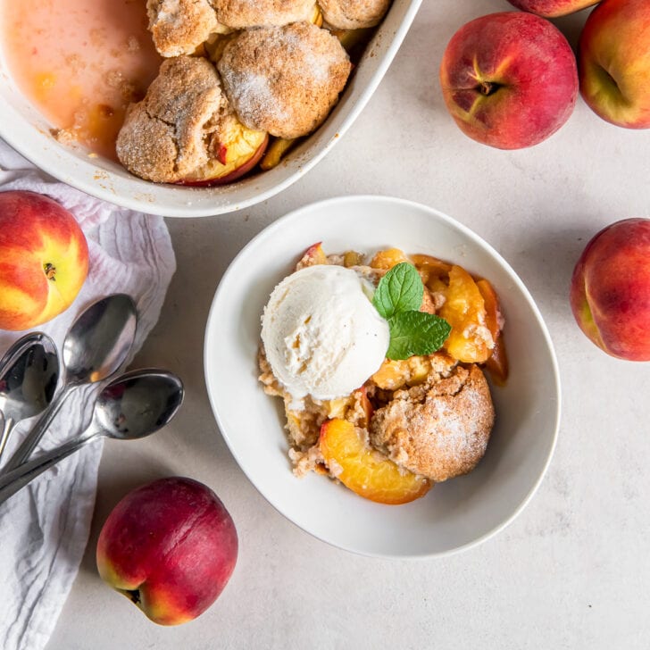 serving of peach cobbler in a white bowl with a scoop of vanilla ice cream.