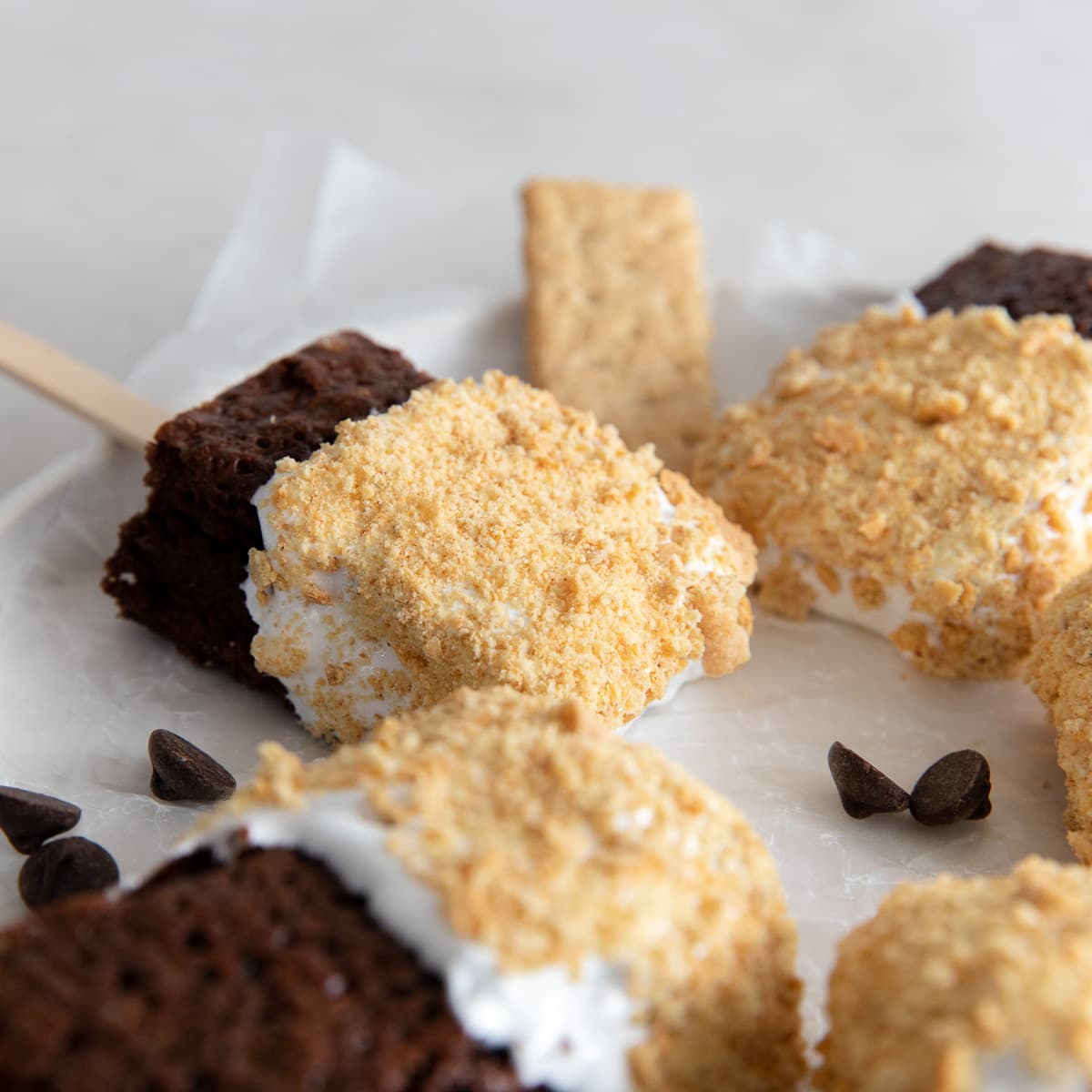 brownies coated in marshmallow fluff and graham cracker crumbs on a stick on a plate.