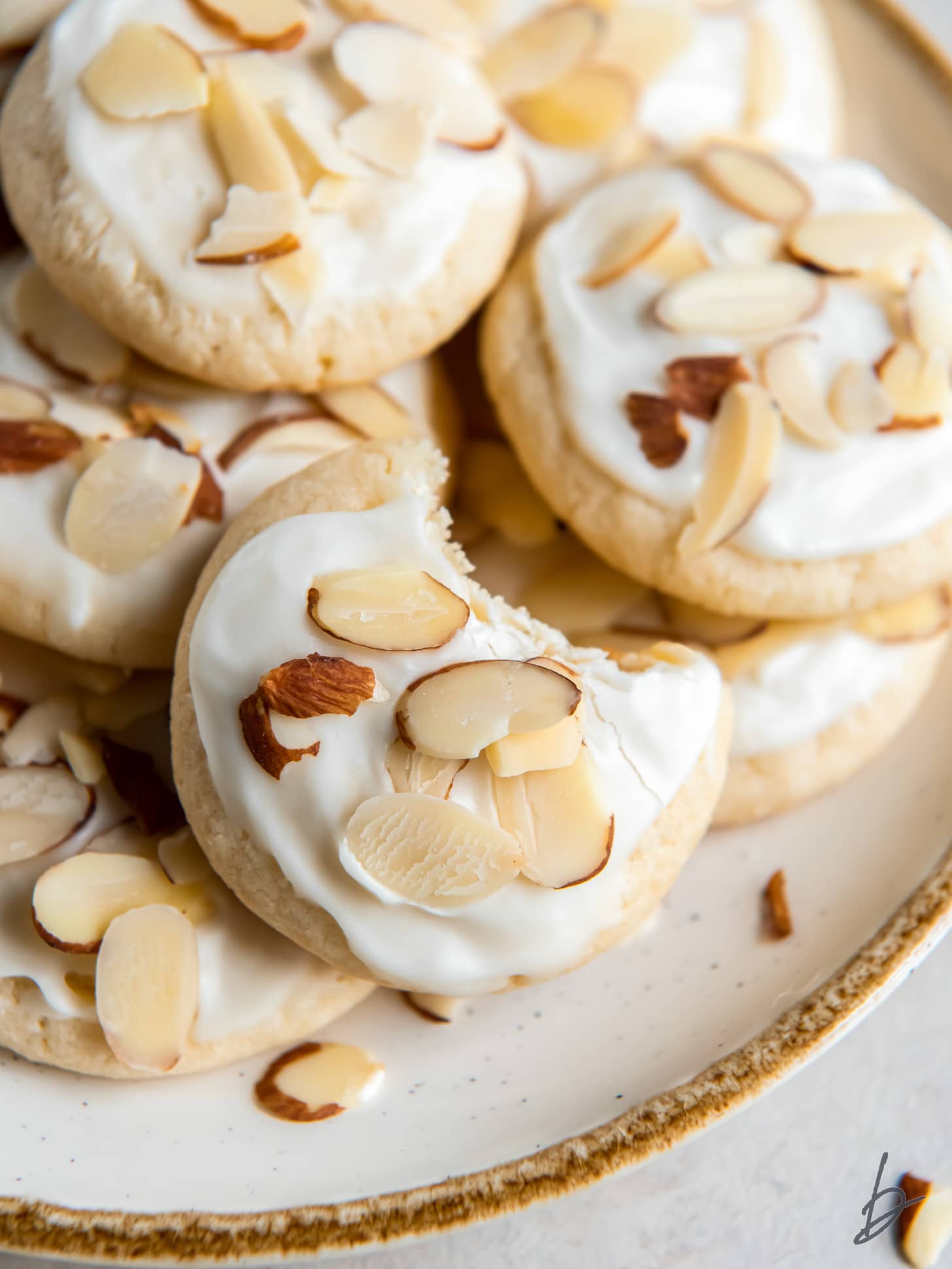 almond sugar cookies with a bite on a plate with more cookies.