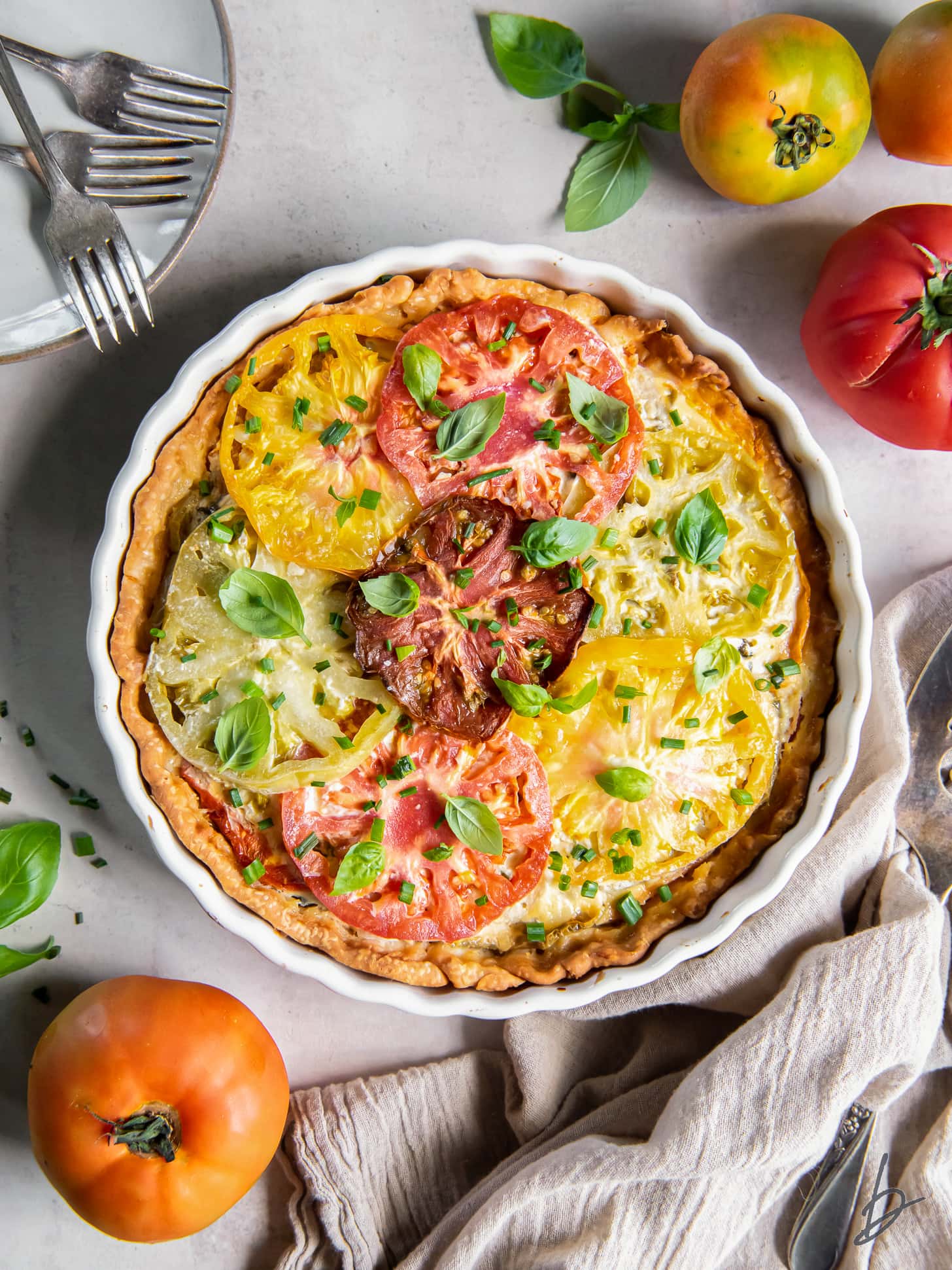 tabletop with southern tomato pie next to fresh heirloom tomatoes.