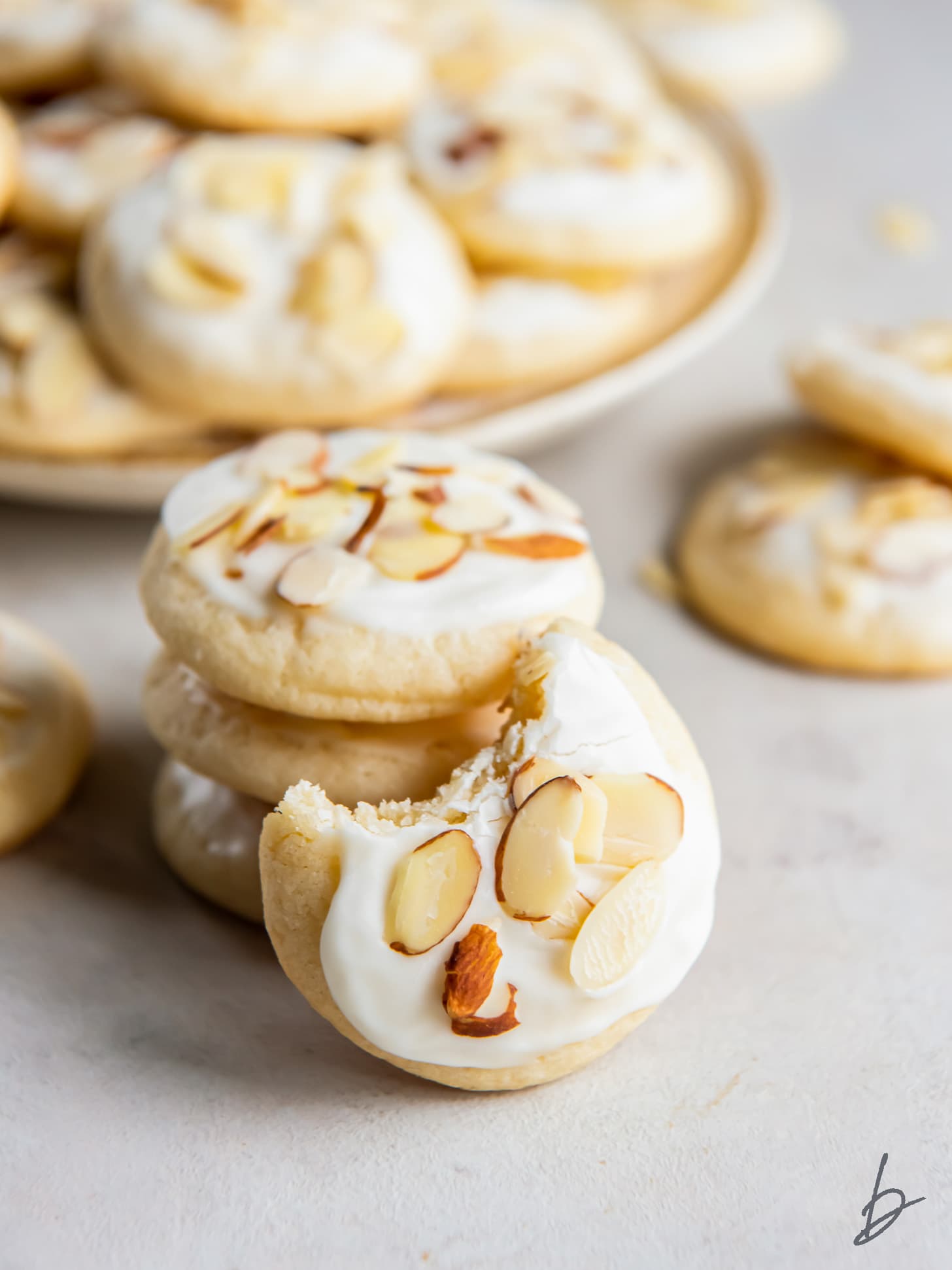 iced almond sugar cookie with a bite leaning against stack of cookies.