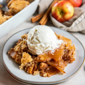 serving of apple cobbler on a plate with a scoop of vanilla ice cream.