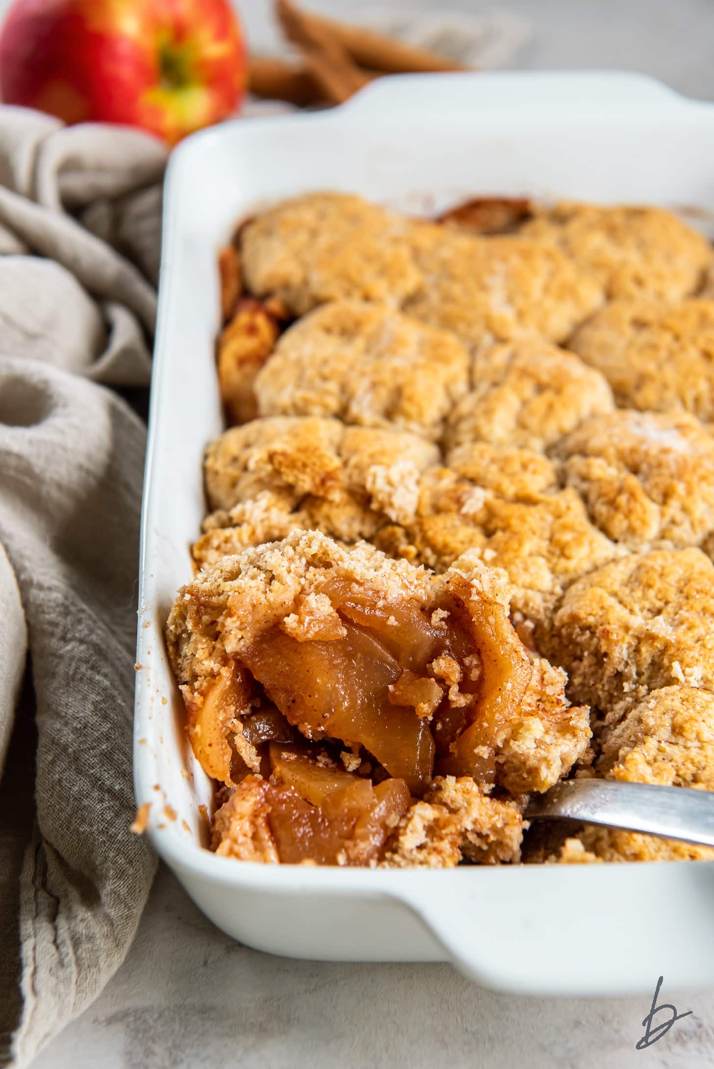 serving spoon taking scoop of apple cobbler from a baking dish.