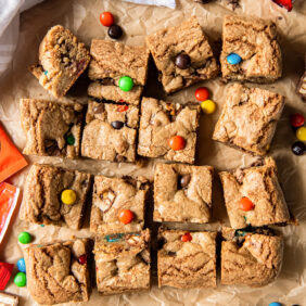 halloween candy cookie bars cut into squares on parchment paper next to more candy.