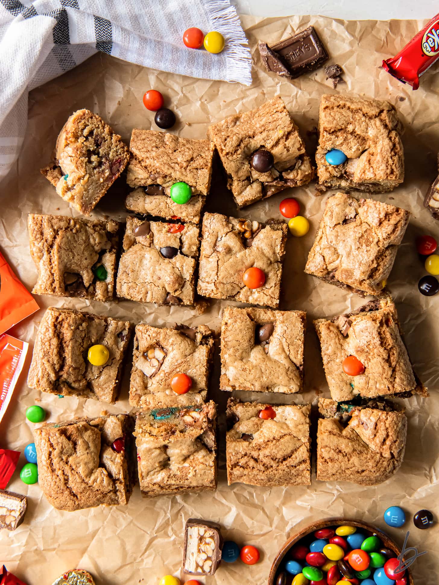 halloween candy cookie bars cut into squares on parchment paper next to more candy.