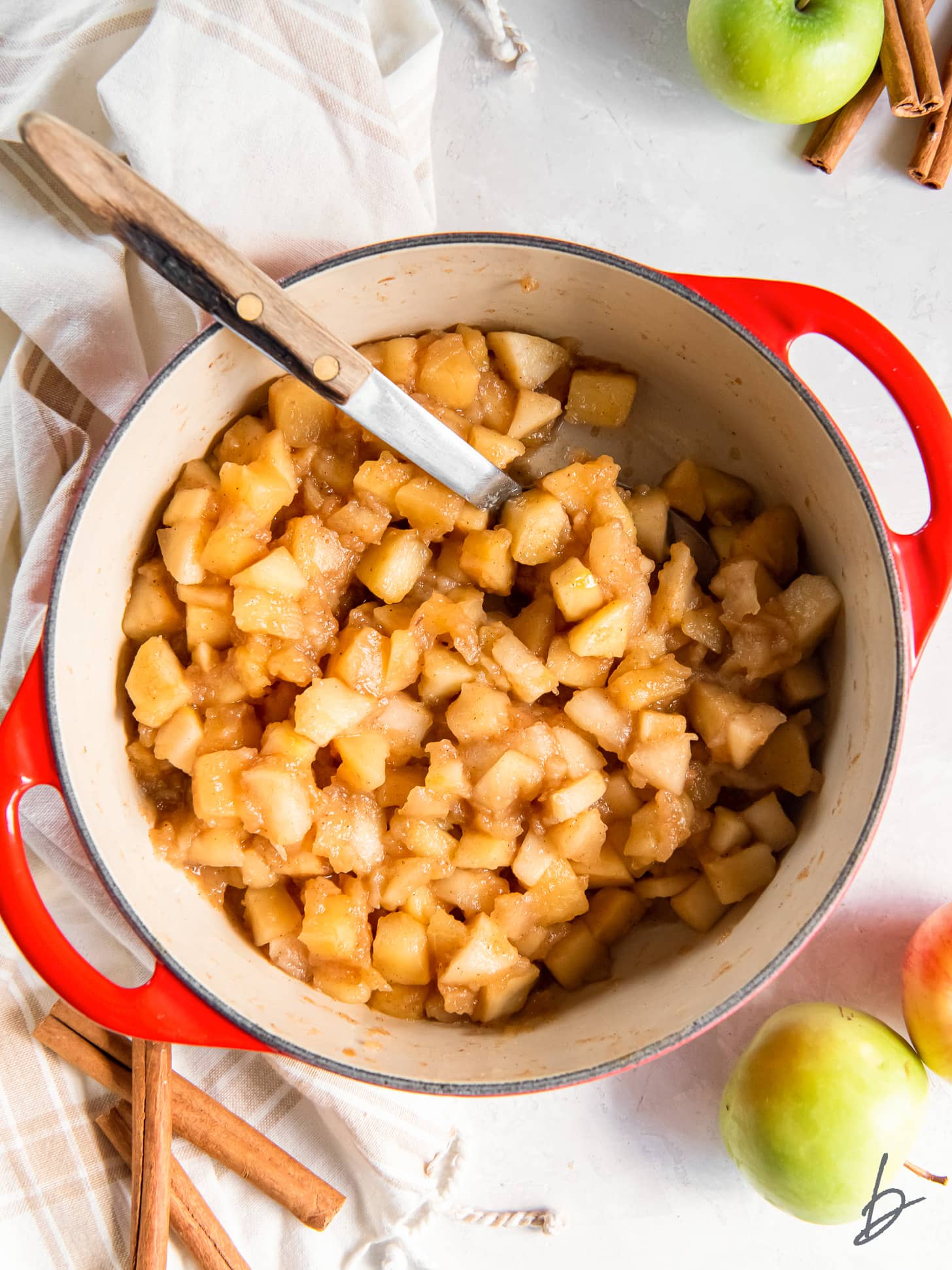 apple compote in a dutch oven with a large spoon.