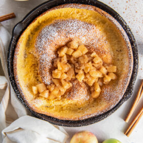 apple dutch baby in a skillet with hand wrapped with kitchen towel.