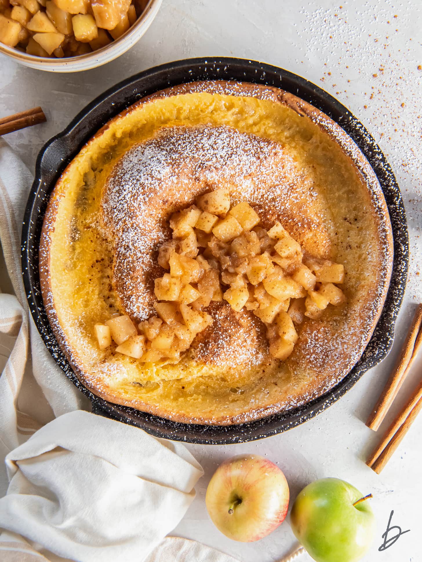 apple dutch baby in a cast iron skillet with hand wrapped with kitchen towel.