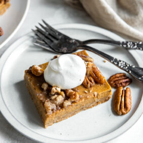 pumpkin pecan pie bar with a dollop of whipped cram on a plate with a fork.