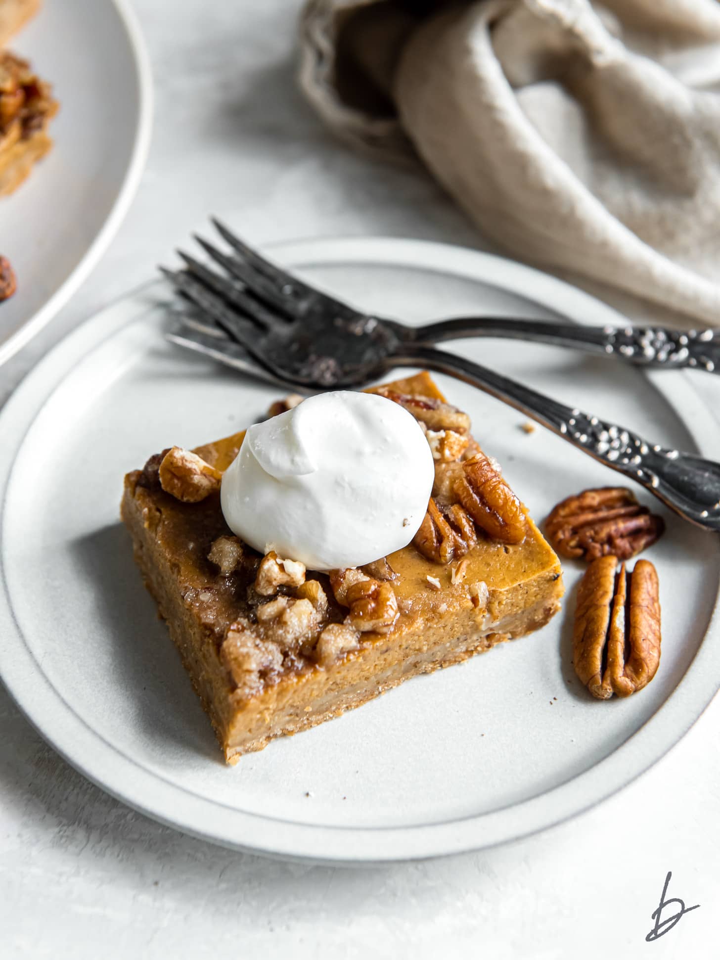 pumpkin pecan pie bar with a dollop of whipped cram on a plate with a fork.