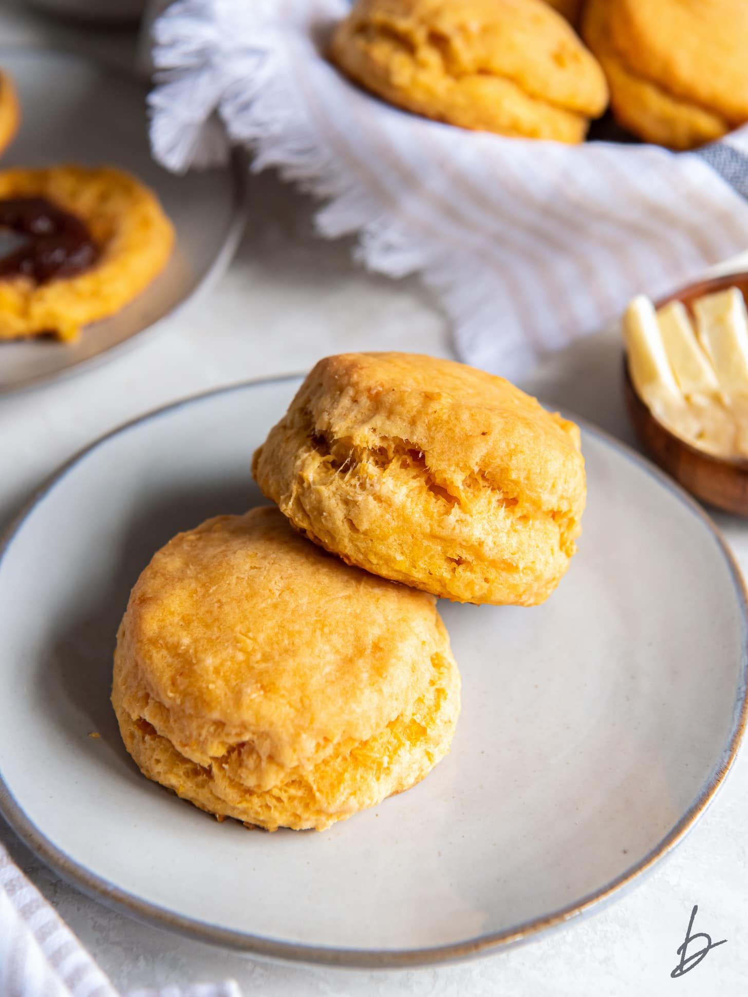 sweet potato biscuit leaning on another biscuit on a plate with small bowl of butter behind it.