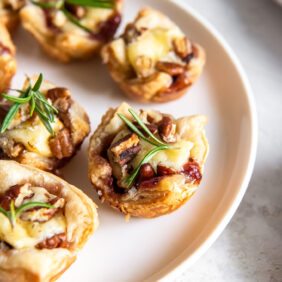 cranberry brie bites on a plate with rosemary garnish.