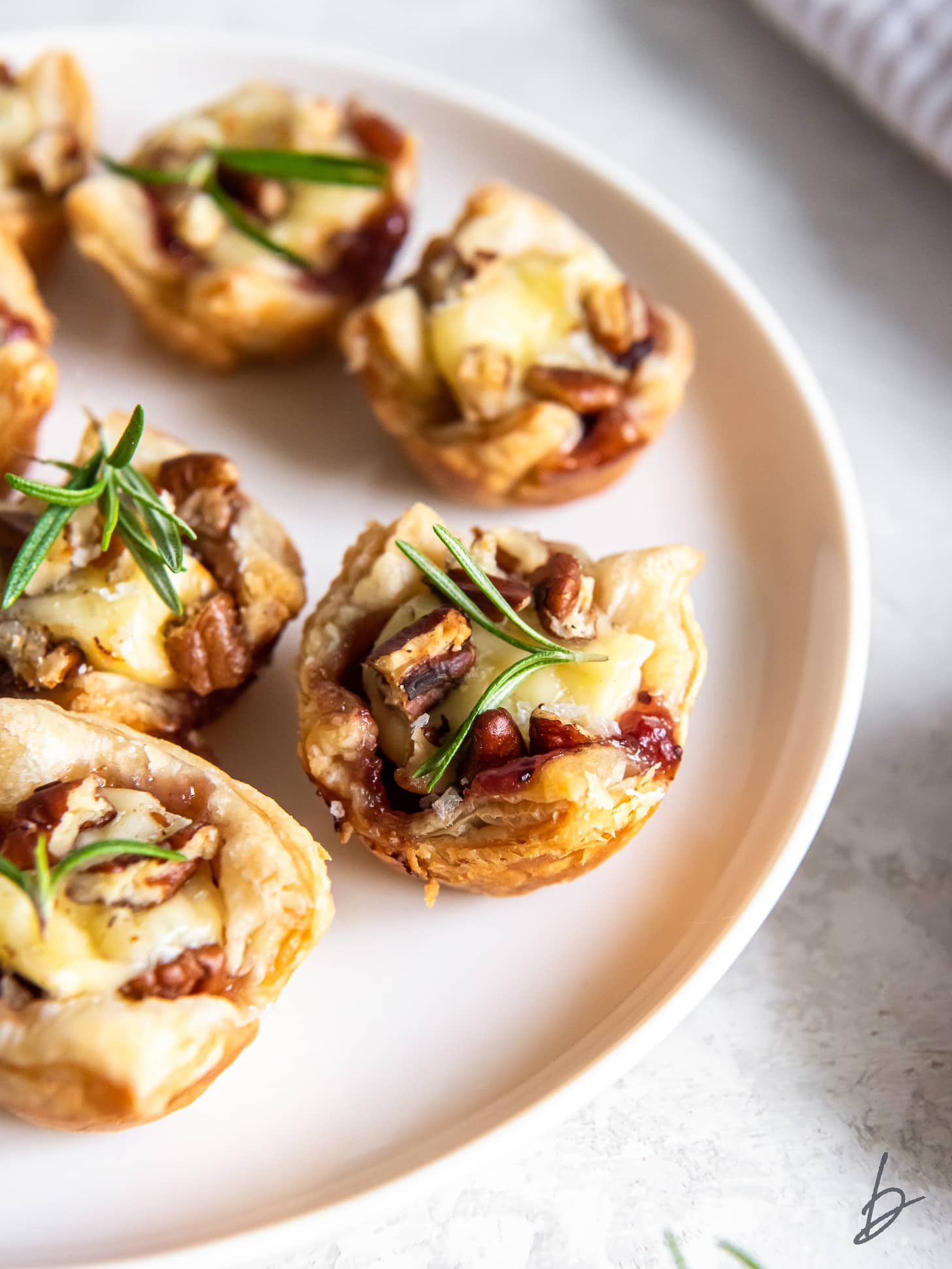 cranberry brie bites on a plate with rosemary garnish.