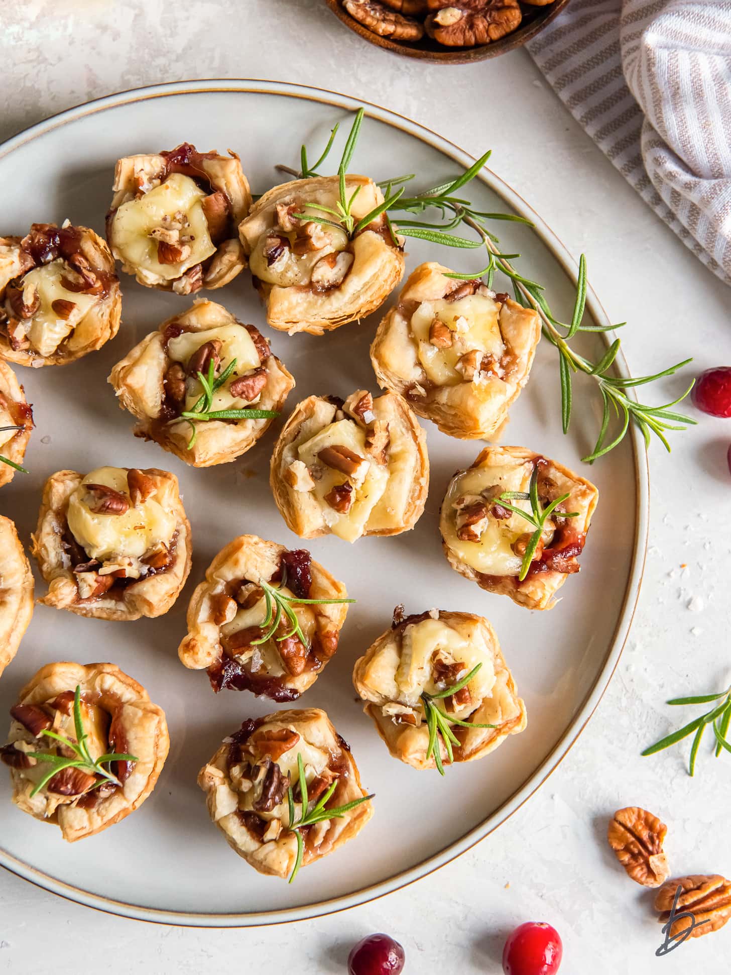 plate of cranberry brie bites with pecans and rosemary garnish.