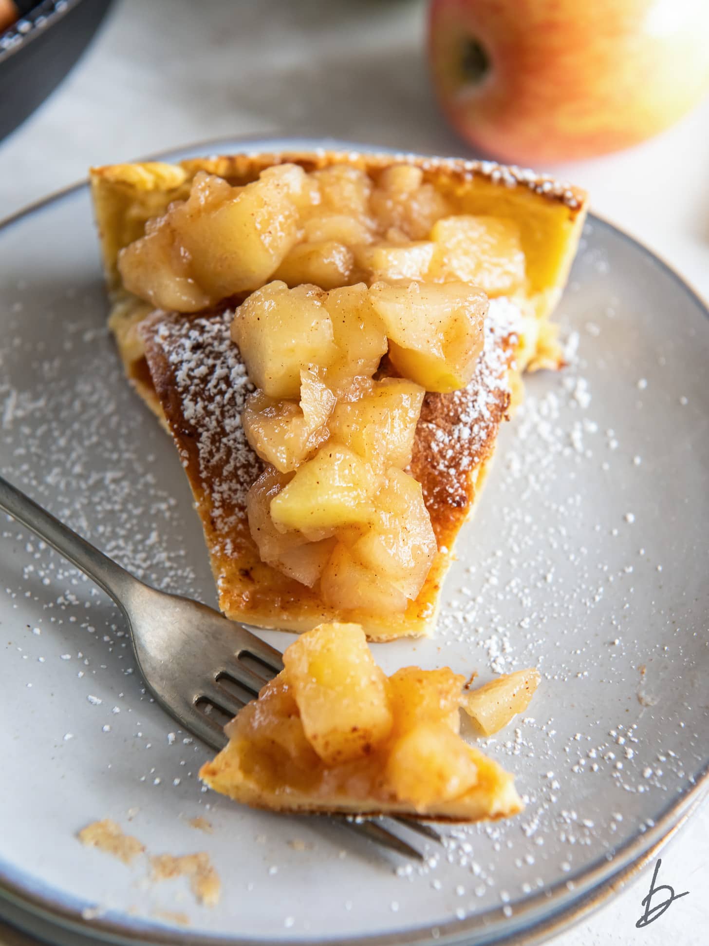 fork hoding bite of dutch baby with apples and dusting of pwodered sugar.