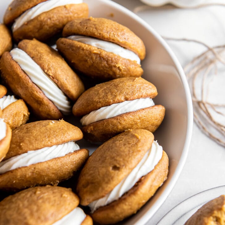 a shallow white bowl with pumpkin whoopie pies with cream cheese filling.