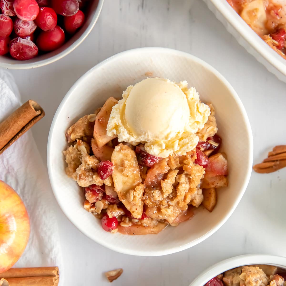 bowl of apple cranberry crisp with a scoop of vanilla ice cream.
