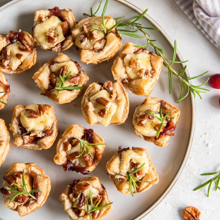 plate with baked brie bites garnished with rosemary and pecans.