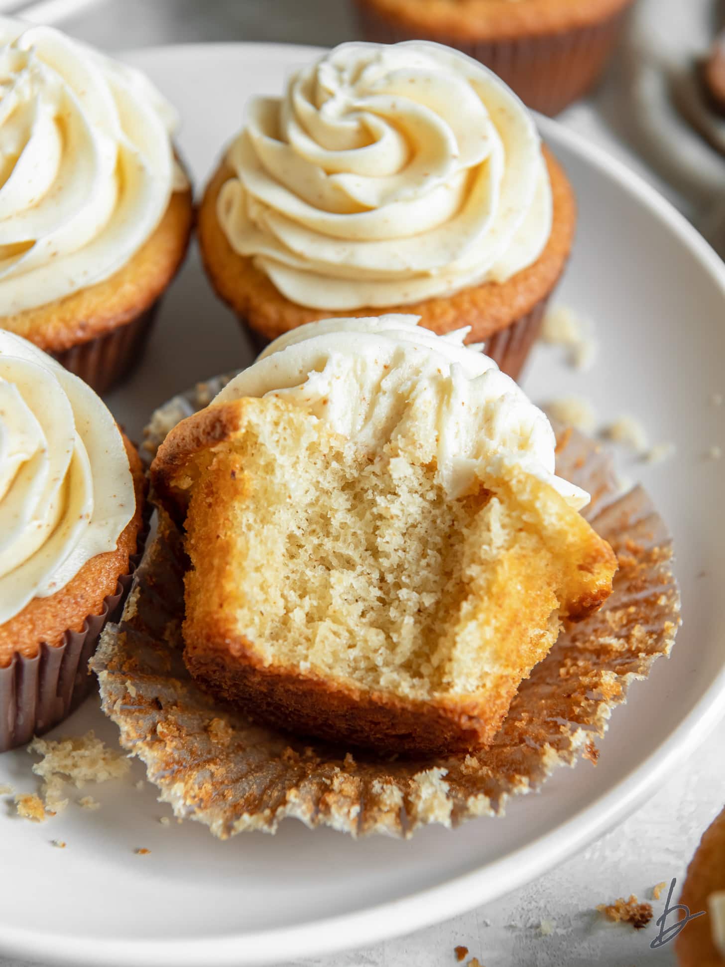 brown butter cupcake with a bite taken out of it leaning on more cupcakes on a plate.