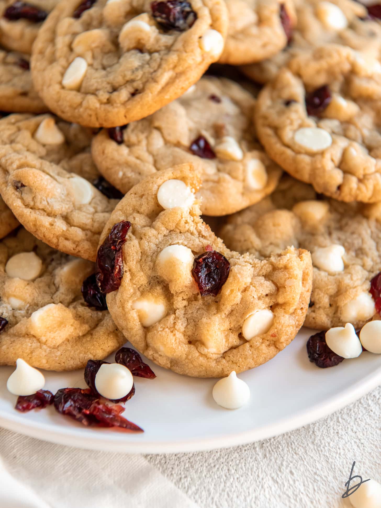 white chocolate cranberry cookie with a bite leaning on more cookies.