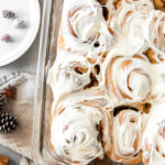 pan of gingerbread cinnamon rolls topped with cream cheese frosting.