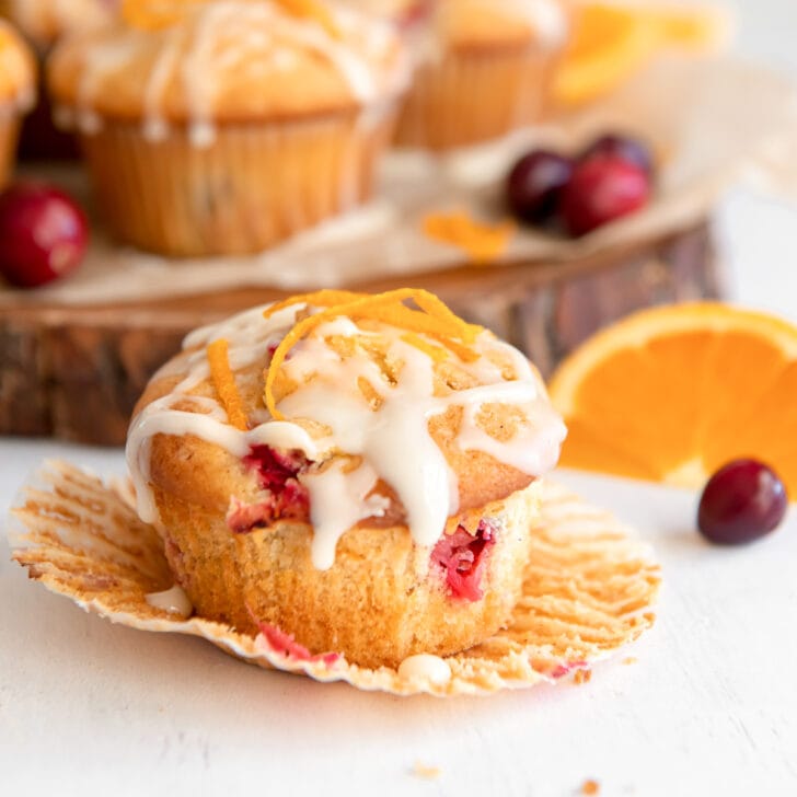 cranberry orange muffins with glaze sitting on an open paper liner.