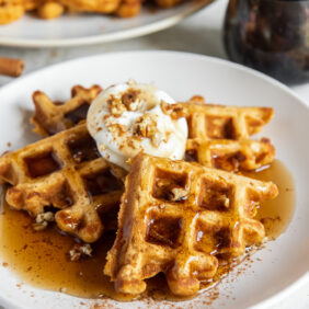 plate of sweet potato waffle triangles with maple syrup and dollop of whipped cream.