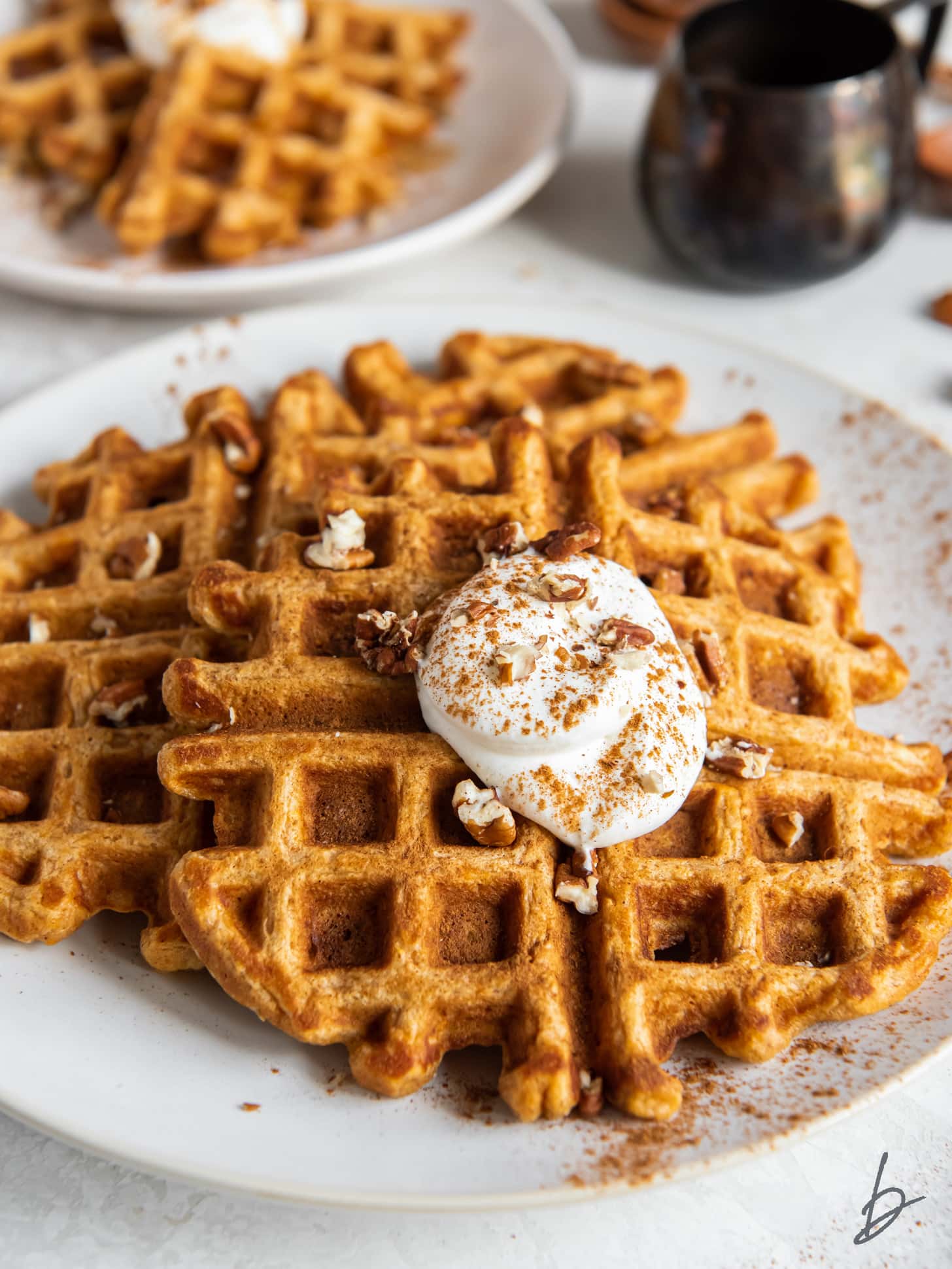 plate with a few sweet potato waffles topped with a dollop of whipped cream and a sprinkle of chopped pecans.