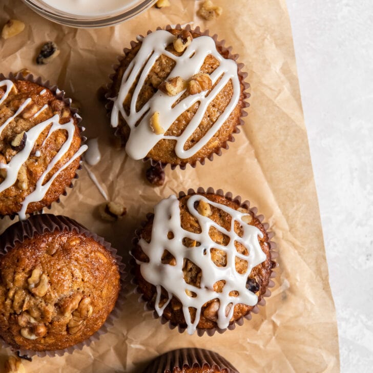 a couple maple muffins topped with icing drizzle on a piece of parchment paper.