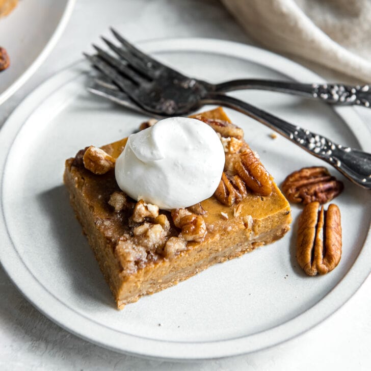 pumpkin pecan pie bar with dollop of whipped cream on a plate with two forks.