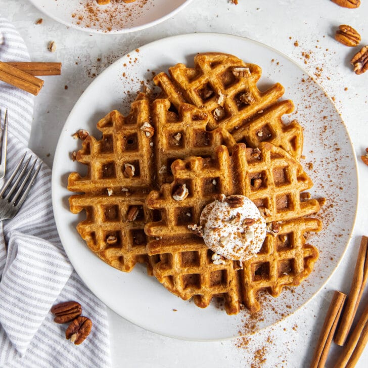 plate of sweet potato waffles with dollop of whipped cream and chopped pecans on top.