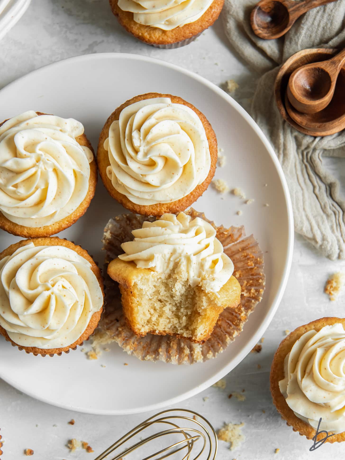 four brown butter cupcakes on a plate with one cupcake on its side with a bite taken out of it.