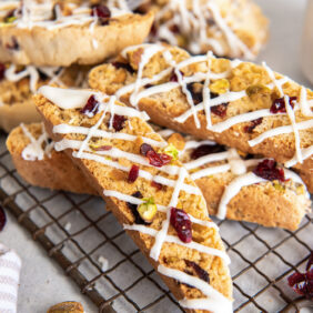 cranberry pistachio biscotti drizzled with white chocolate in a pile on a wire rack.