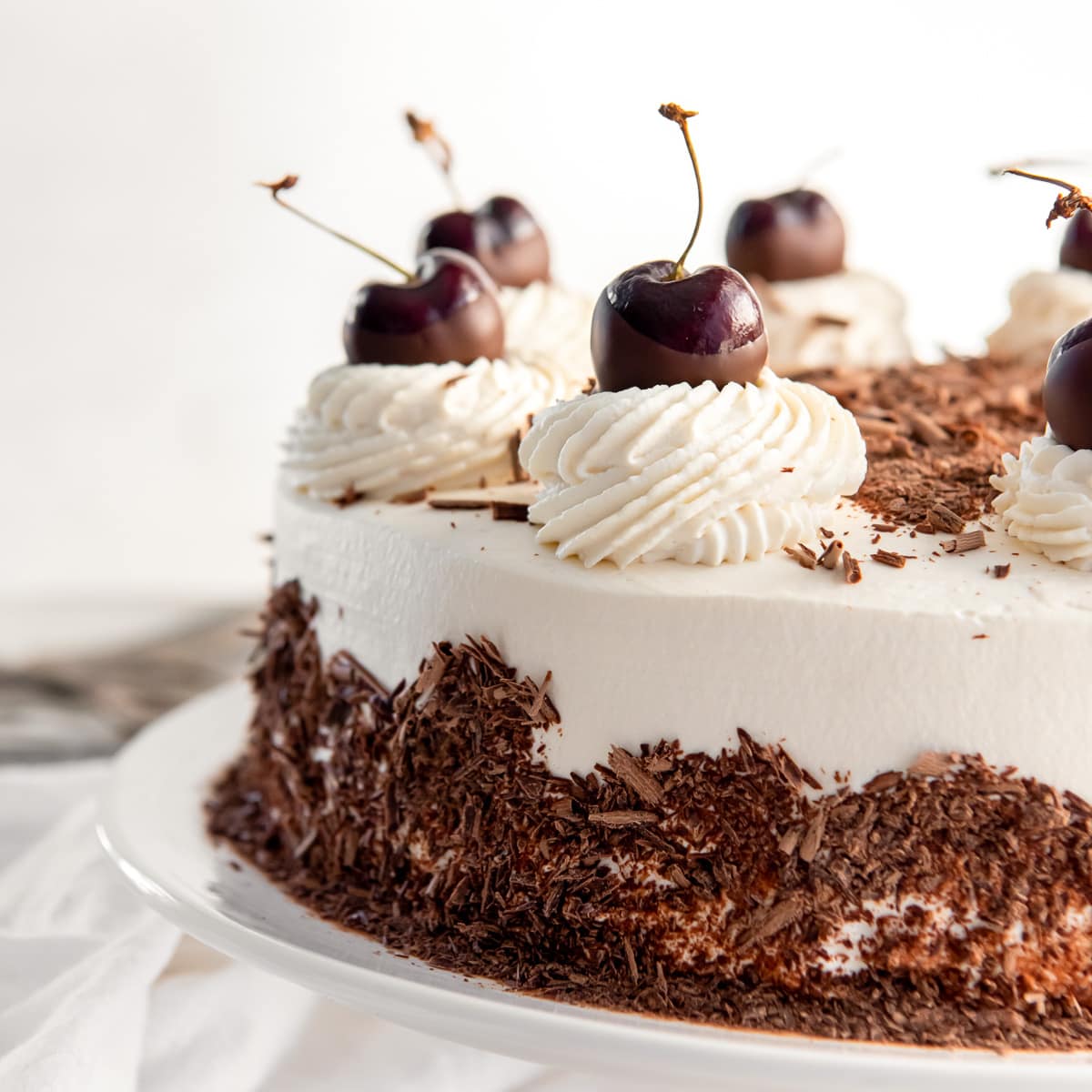 black forest cake with whipped cream frosting, chocolate shavings and dark cherries for garnish.