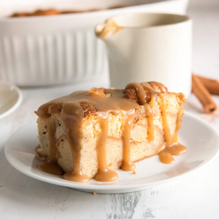 piece of bread pudding on a plate with bourbon sauce dripping down the sides.