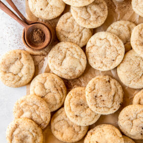 many eggnog snickerdoodles on parchment paper next to teaspoon of ground nutmeg.