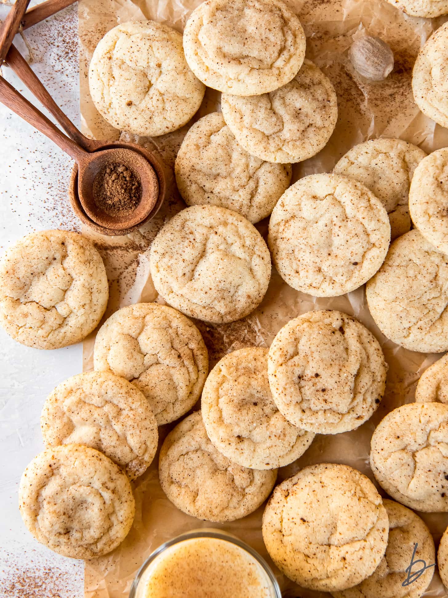 many eggnog snickerdoodles on parchment paper next to teaspoon of ground nutmeg.