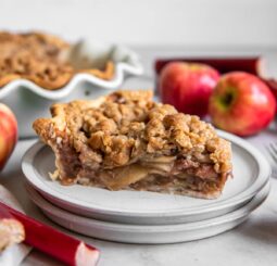 slice of apple rhubarb pie with crumble topping on a plate.