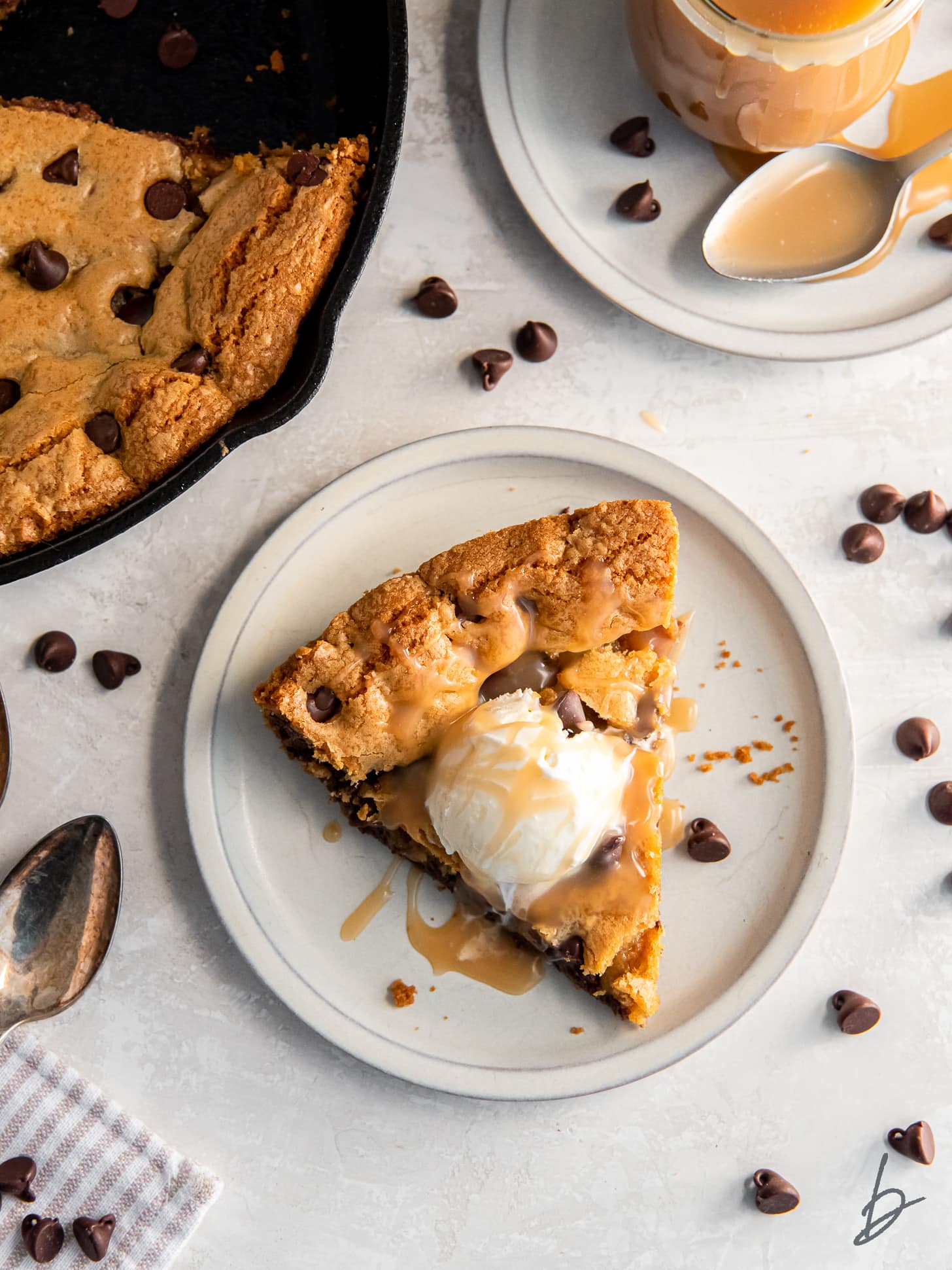 slice of a chocolate chip skillet cookie on a plate with a scoop of vanilla ice cream and drizzle of caramel.