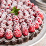 chocolate raspberry tart on a plate with confectioners' sugar dusted on top of the raspberries.