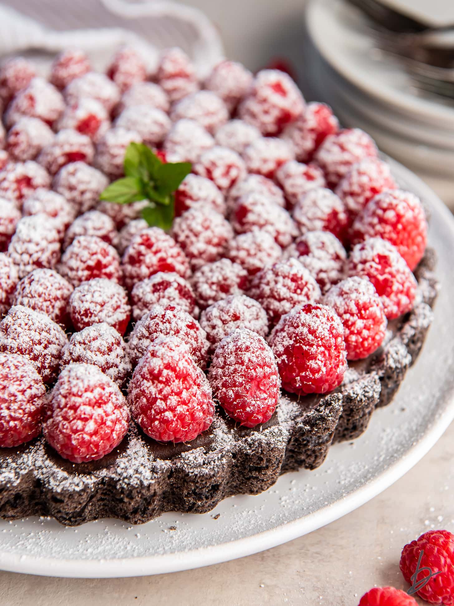 chocolate raspberry tart on a plate with confectioners' sugar dusted on top of the raspberries.