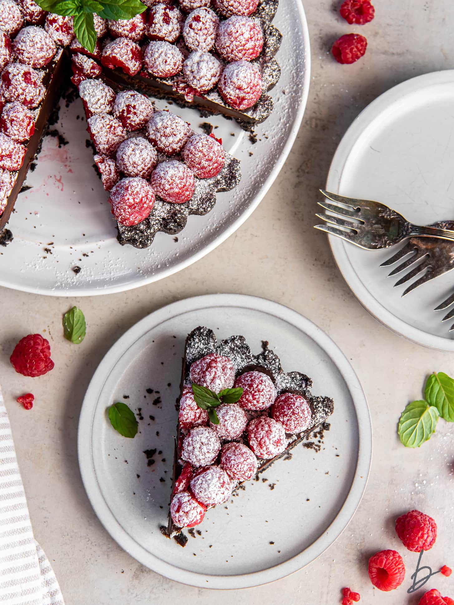 slice of chocolate raspberry tart on a plate next to the whole tart dusted with confectioners' sugar.