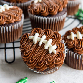 football cupcake topped with chocolate frosting and vanilla frosting stitched laces.
